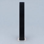 A tall, narrow black rectangular stand or post with a square silver metal base, centered against a light gray studio background.